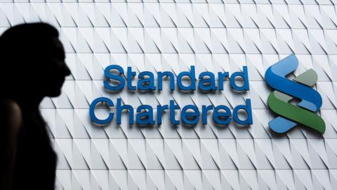 A woman walks past a logo of the Standard Chartered bank in Hong Kong on August 5, 2015