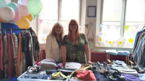 Two ladies smiling in front of loads of clothes and donations
