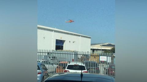 An air ambulance flying over grey buildings on an industrial estate.