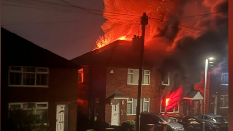 Billowing smoke and flames as the fire burned at the house. Large orange cloud of smoke rises high into the dark sky.