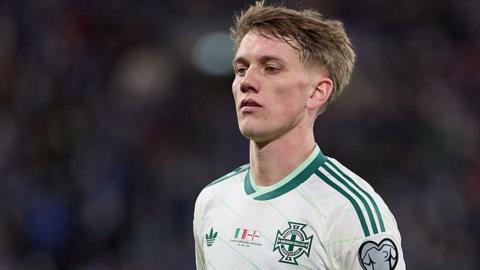 Ethan Galbraith in action for Northern Ireland. He is wearing a white and dark green trimmed away shirt.