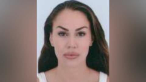 A woman with long brown hair is wearing a white vest