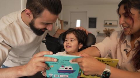 Jasmin and Hasnain Bashir read through a children's book with their son Eliyas, who is in an assisted chair.