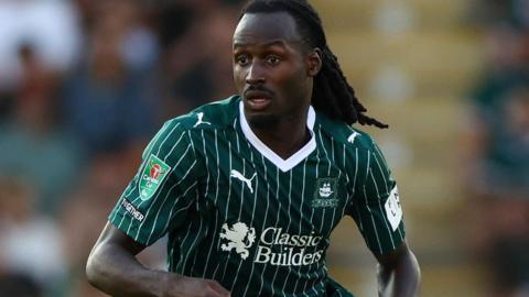 Malachi Boateng playing in the green and white pin stripe Plymouth Argyle kit. He has long black hair.