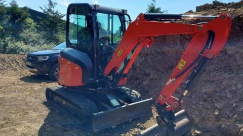 An orange digger which is behind a large mound of dry brown mud.