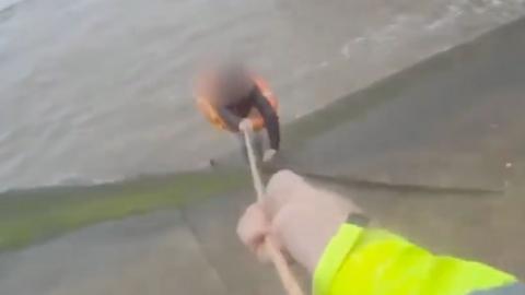 Bodycam footage showing a woman with a life ring round her waist being dragged up a wet concrete bank away from the sea, and the arms of a police officer in high vis pulling on a rope attached to the ring