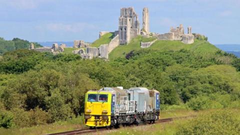 A  Multi Purpose Vehicle on rail tracks with the ruins of Corfe Castle in the background