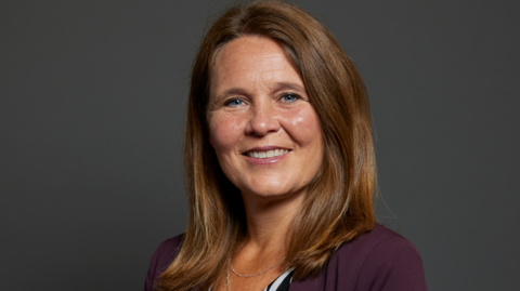 Official Parliamentary portrait of MP Vikki Slade. She has shoulder length chestnut-brown hair and is wearing a deep-purple jacket.