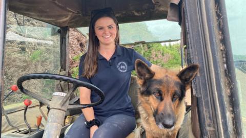 Bethany Sharpe sitting in a tractor with her arm around her Alsatian dog,  Willow 