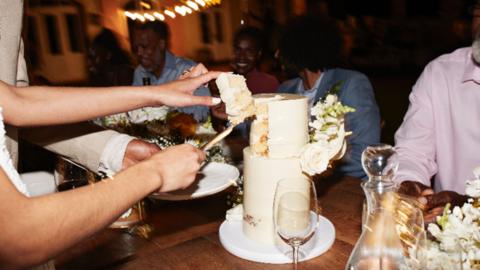 A wedding cake being cut with a wine glass next to it on the table.
