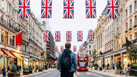 A man standing in the middle of Oxford Street with union jack flags hanging above