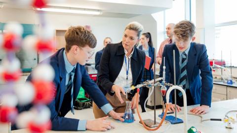 Two GCSE students and their teacher conducting an experiment in chemistry in a school lab.