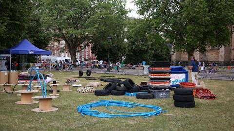 Play equipment including blue pipes, cardboard and tyres, lying on grass in playground.