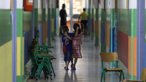 Two children walk arm in arm down a long, colourful corridor