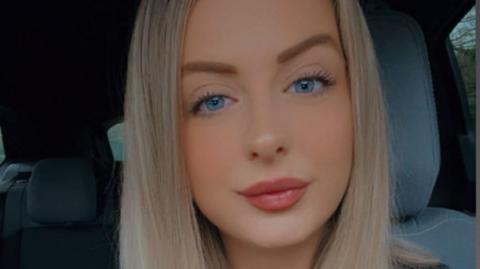 Woman with long blonde hair smiles slightly at the camera