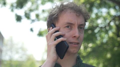A man holds his phone up to his ear looking