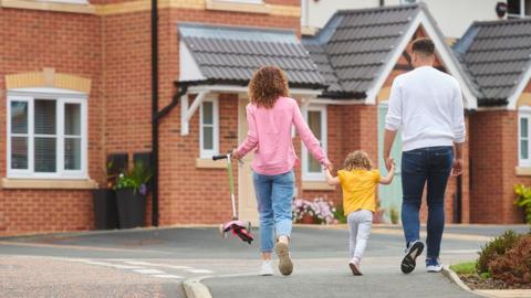 Family holding hands walking on a housing estate with flowers dotted around