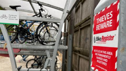 A sign says "Thieves Beware" in front of bikes on a bike rack.