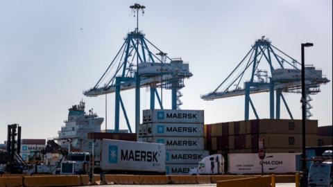 Several shipping containers are seen on trucks and stacked on piers and cranes at a port in Philadelphia