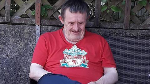 Photo of William John Jones who had down syndrome. He is an elderly man with brown hair. He is wearing a Liverpool FC t-shirt