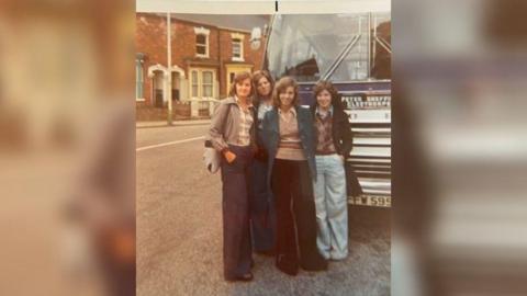 Four teenage girls standing in front of a coach in 1975