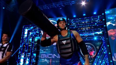 Bionic from Gladiators poses in the arena holding a prop and wearing a bodysuit 