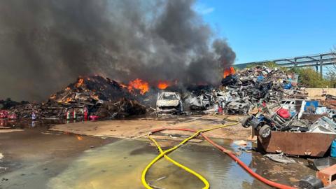 Hoses on the floor in front of a heap of burning scrap