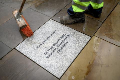 A man sweeps a brush over the newly paved tribute stone to Fred Dibnah