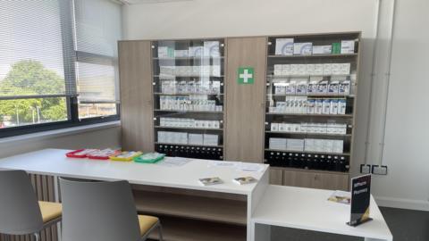 A large cabinet in a classroom has medicines behind glass doors.