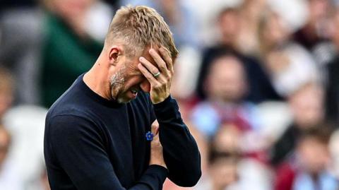 Graham Potter with a raised left hand partly covering his face, looking frustrated