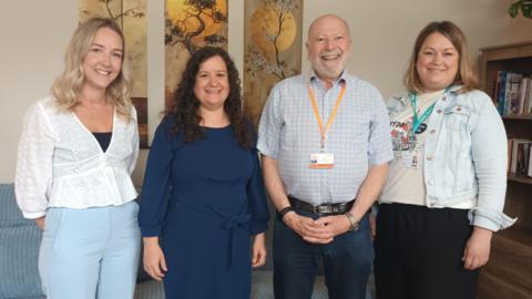 Four people stand in a room, three women and a man. They are Kayleigh Jones, Missing Link Service Manager for Oriana House, Sarah O’Leary, Missing Link CEO, Councillor Neil Hopkins, Swindon Borough Council, and Helen Brian, Albare Head of Mental Health. They are standing in a line smiling at the camera.