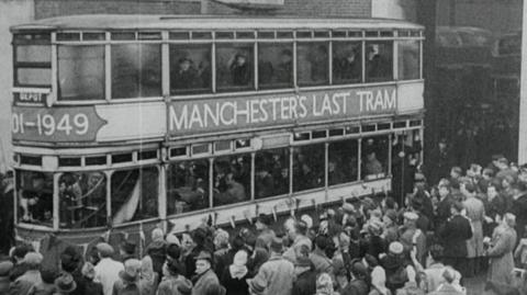 Black and white image of Manchester tram returning to base surrounded by a waiting crowd.  a sign on the side says "Manchester's Last Tram'.