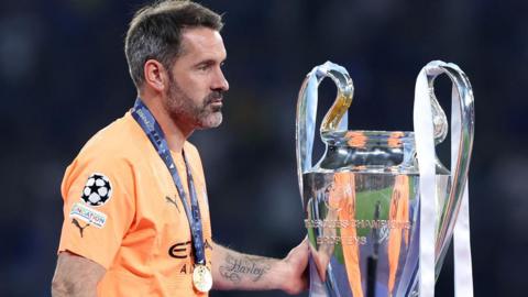 Scott Carson touches the Champions League trophy after Manchester City complete the Treble in 2022-23