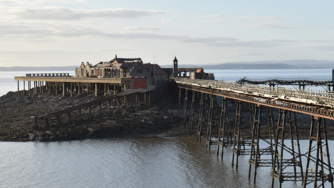 Looking across to Birnbeck Pier from the shore on an overcast day. The pier is dilapidated and looks neglected