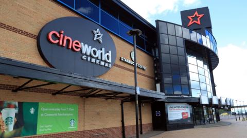 The outside of a Cineworld Cinema complex. A logo of the company is on the outside of the building which is a black oval with a white star and red and white writing which says cineworld CINEMAS.