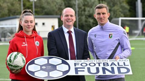 Communities Minister Gordon Lyons pictured with Marcus Kane from Glentoran and Naomi McLaughlin from Cliftonville