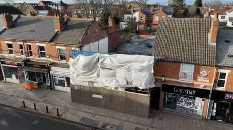 A drone image showing a row of properties - the aerial shot shows that two buildings in the middle of the terraced street have been demolished. Scaffolding covers the front of where the buildings were.