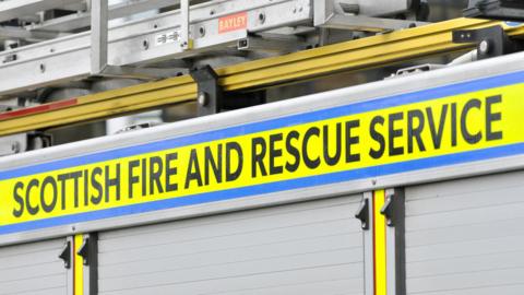 The side of a fire engine with the Scottish Fire and Rescue Service name in black lettering on a bright yellow background