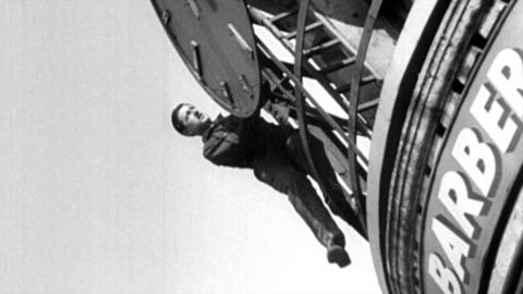 Black and white image of a man hanging off the top of a London West End nightspot, fixing lights and listings to the top of a building.