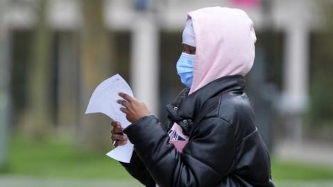 A woman in a pink hoodie holds a piece of paper as she queues for antibiotics
