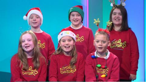 A group of choir children smile at the camera and sing in the Newsround studio.