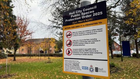 A Public Spaces Protection Order (PSPO) sign. The blue, yellow and white signs lists the restrictions under the order and has the logos of the city council, Humberside Police and the NHS at the bottom.