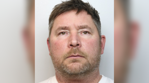 A custody mugshot of Craig Arrowsmith. He has a short, stubbly beard and white T-shirt.