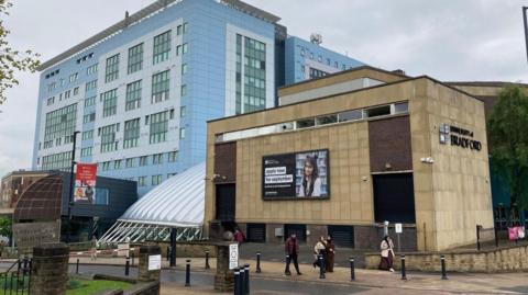 Two large buildings with people walking past. One of the buildings has a sign saying "University of Bradford". 