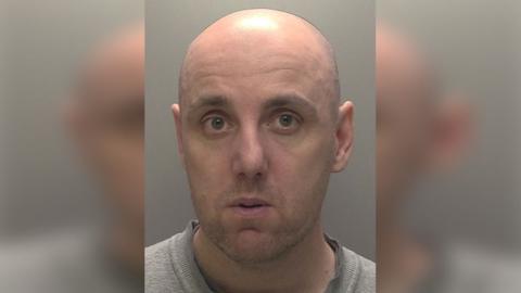 Police custody photograph of David Brennan who is bald and is wearing a grey top