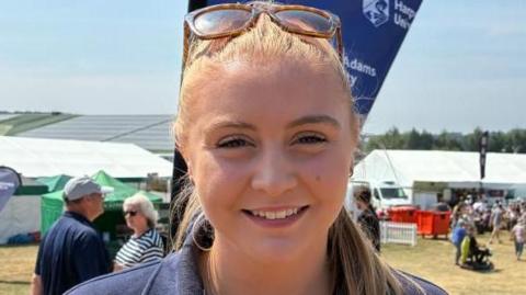 A woman with blond hair smiles as her sunglasses sit on the top of her head.