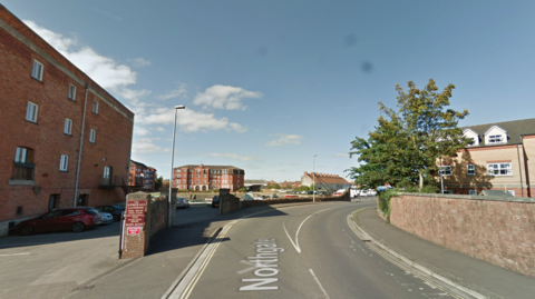A road with houses on both sides. It is sunny and the sky is blue.