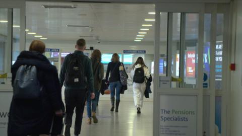 Passengers walking through automatic doors in Jersey airport towards the customs area.