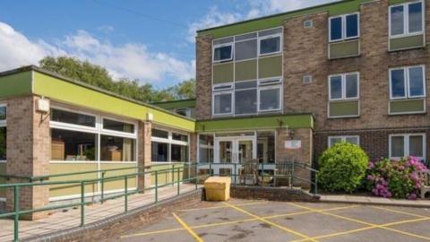 The front of a brick building with green features near the roof and windows - it is the former Sidney Gale Care Home