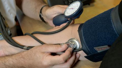 A close up image of a doctor measuring a patient's blood pressure and heart beat.